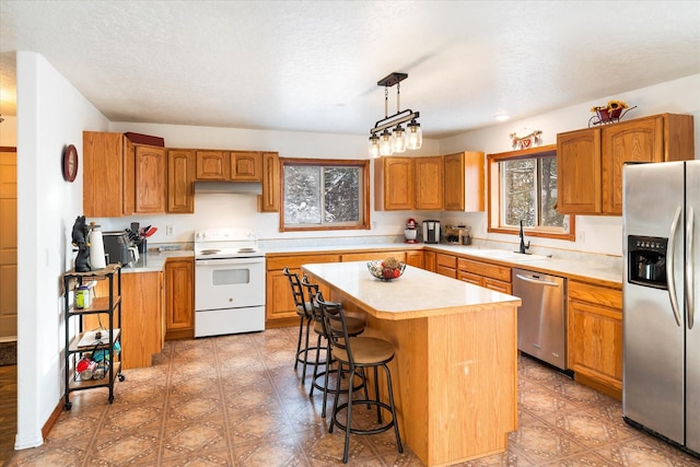 kitchen featuring appliances with stainless steel finishes, a center island, light countertops, under cabinet range hood, and a sink