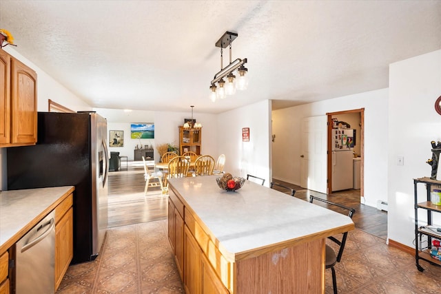 kitchen with a breakfast bar area, light countertops, appliances with stainless steel finishes, a kitchen island, and a textured ceiling