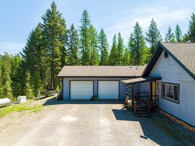 view of front facade with dirt driveway, a shingled roof, and a garage