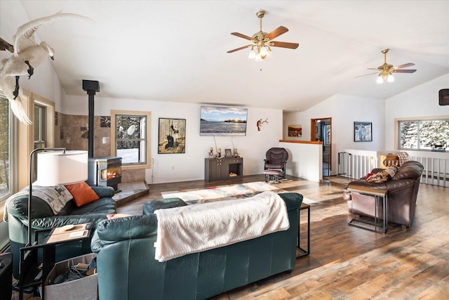 living area with a wood stove, plenty of natural light, vaulted ceiling, and wood finished floors