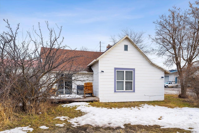 snow covered property with roof with shingles, a chimney, and a wooden deck