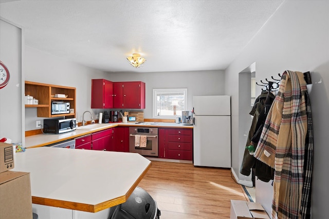 kitchen with light wood finished floors, red cabinets, appliances with stainless steel finishes, light countertops, and a sink