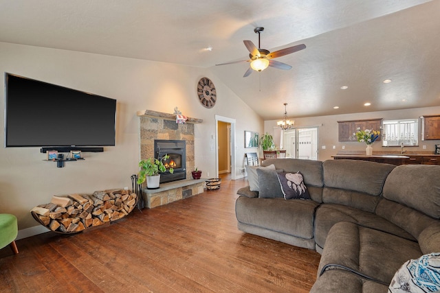 living area with lofted ceiling, ceiling fan with notable chandelier, a fireplace, and wood finished floors