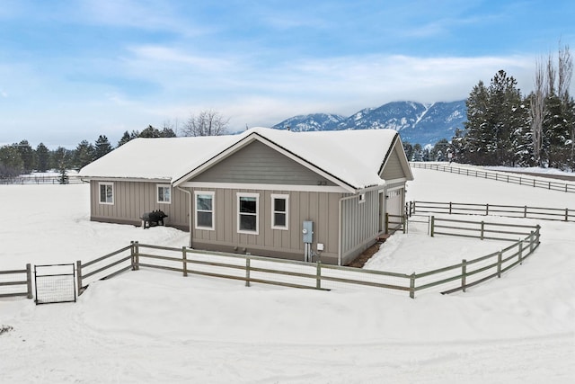 snow covered house featuring board and batten siding, fence, and a mountain view