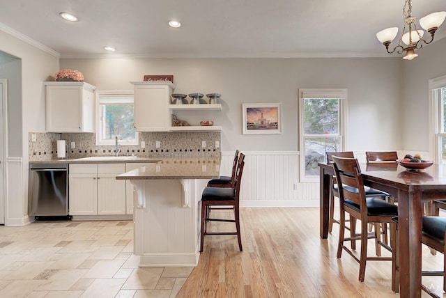 kitchen featuring dishwasher, a wainscoted wall, a breakfast bar area, crown molding, and a sink