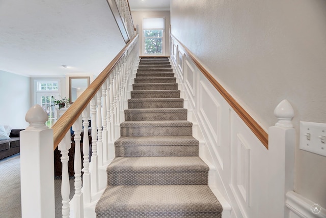 stairs featuring crown molding, carpet, wainscoting, and a decorative wall