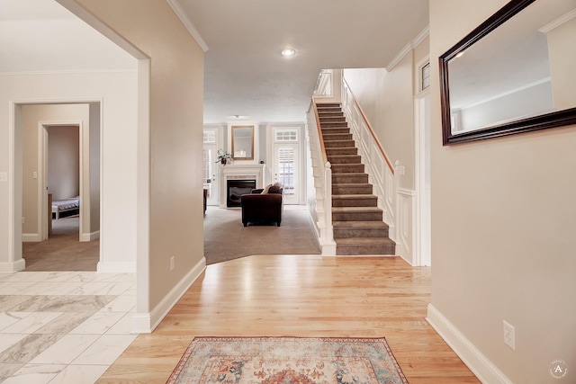 foyer featuring crown molding, a glass covered fireplace, wood finished floors, baseboards, and stairs