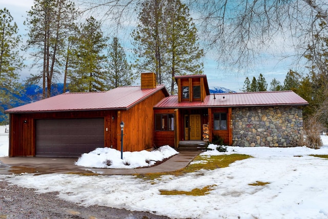 view of front of property with metal roof, stone siding, a chimney, and an attached garage