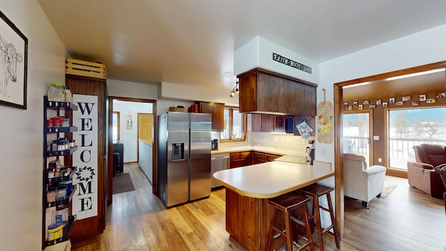 kitchen with decorative backsplash, a peninsula, stainless steel appliances, light countertops, and light wood-style floors