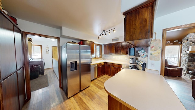 kitchen with appliances with stainless steel finishes, light wood-type flooring, light countertops, and backsplash