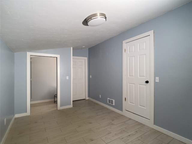 unfurnished bedroom with lofted ceiling, light wood-style flooring, visible vents, baseboards, and a closet