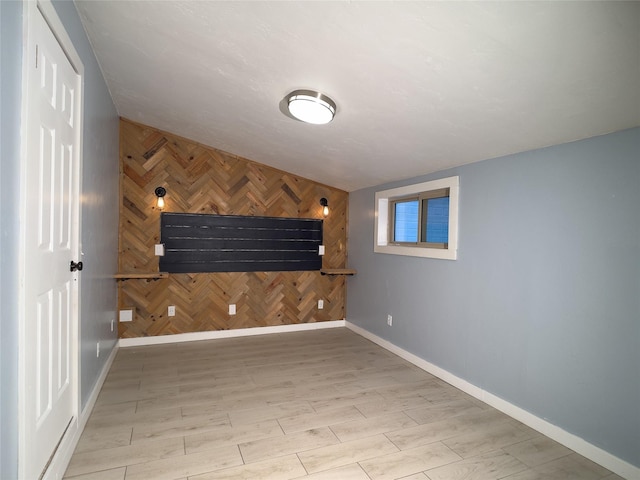 basement with wooden walls, an accent wall, wood finished floors, and baseboards