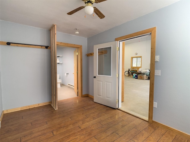 unfurnished bedroom with hardwood / wood-style floors, a baseboard heating unit, ceiling fan, ensuite bath, and baseboards