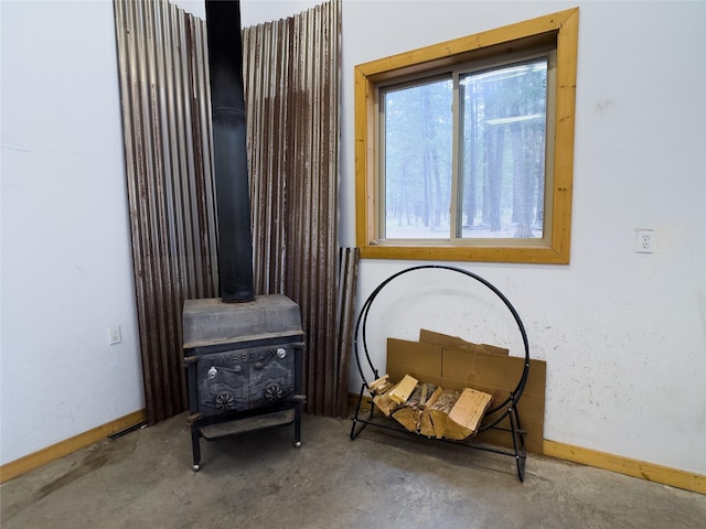 living area featuring a wood stove, baseboards, and unfinished concrete flooring