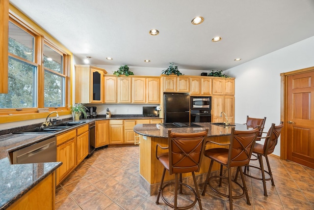 kitchen featuring dark stone counters, glass insert cabinets, a breakfast bar, black appliances, and a sink