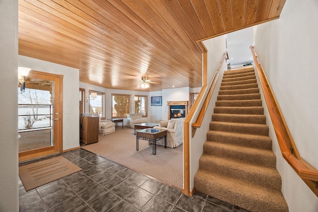 interior space with ceiling fan, a glass covered fireplace, carpet flooring, and wood ceiling