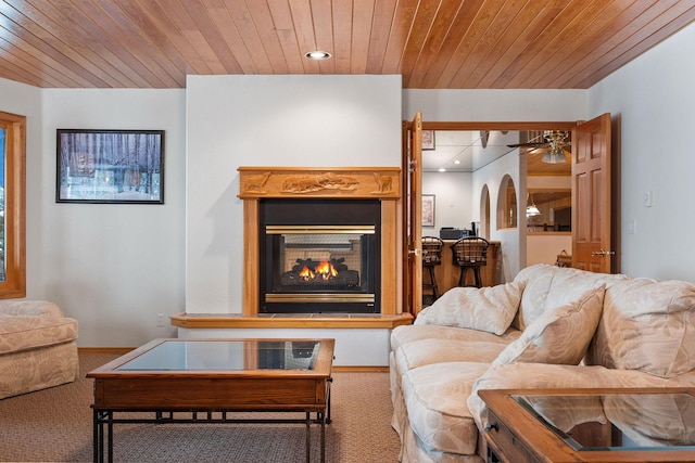 carpeted living area featuring wood ceiling, a lit fireplace, arched walkways, and recessed lighting