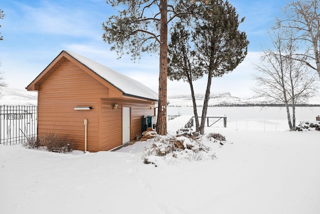 snow covered property featuring a garage, fence, and an outdoor structure