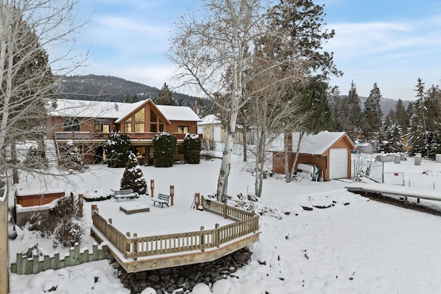 yard covered in snow featuring an outbuilding, a detached garage, and a wooden deck