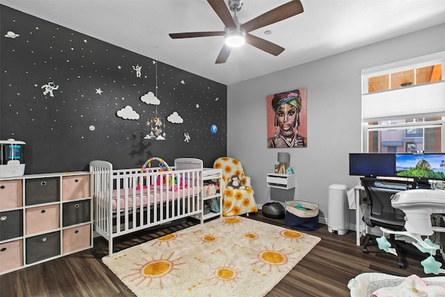 bedroom featuring an accent wall, wood finished floors, baseboards, a nursery area, and wallpapered walls