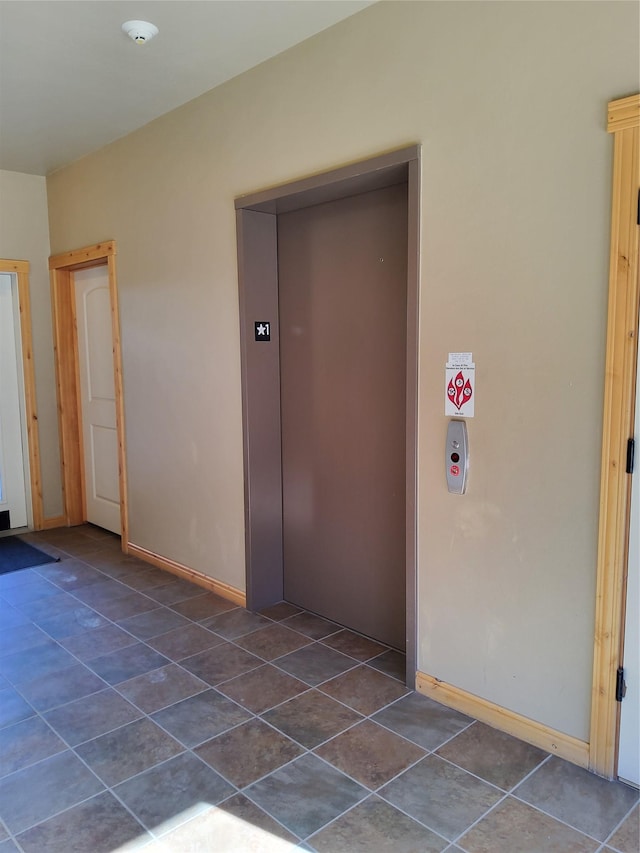 unfurnished room featuring baseboards, dark tile patterned floors, and elevator