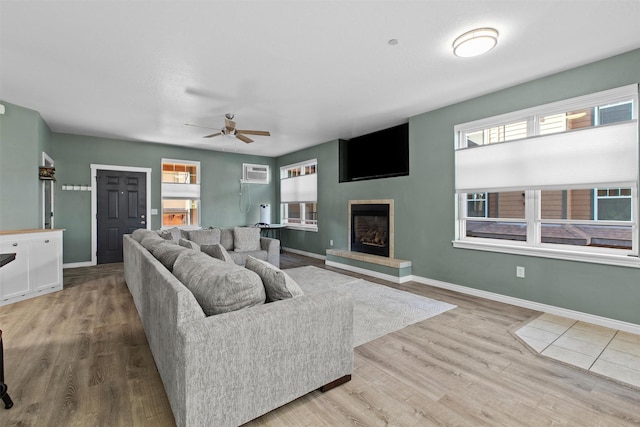 living area with a fireplace with raised hearth, a wall unit AC, baseboards, and wood finished floors