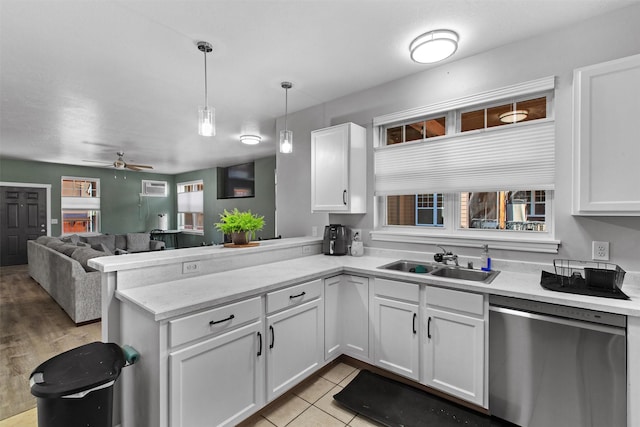 kitchen with a peninsula, stainless steel dishwasher, a sink, and white cabinets