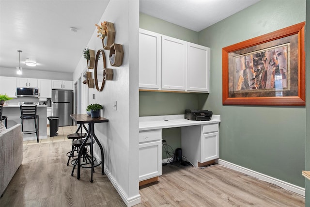 kitchen featuring a breakfast bar area, light wood-style flooring, white cabinetry, appliances with stainless steel finishes, and built in study area