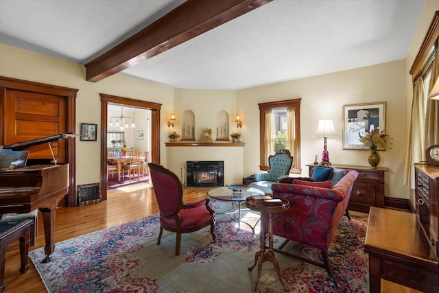 living area featuring beamed ceiling, a fireplace, wood finished floors, and baseboards