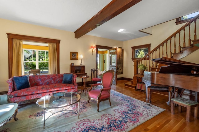 living room featuring wood finished floors, beam ceiling, baseboards, and stairs