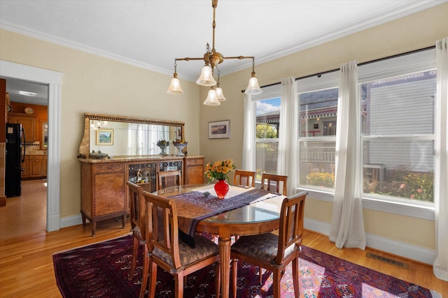 dining space featuring baseboards, light wood finished floors, visible vents, and crown molding