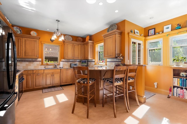 kitchen featuring decorative backsplash, light stone counters, brown cabinets, a peninsula, and a sink