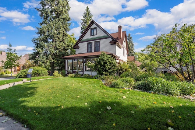 view of front facade featuring a sunroom, a chimney, and a front yard