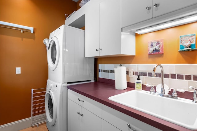 laundry room featuring stacked washing maching and dryer, a sink, cabinet space, and baseboards