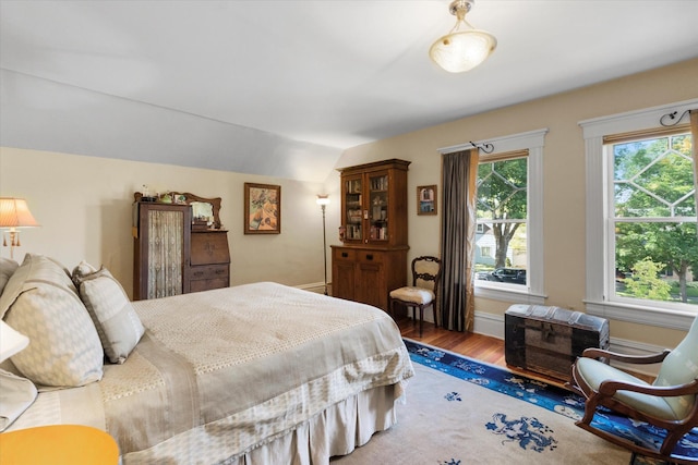 bedroom with multiple windows, baseboards, vaulted ceiling, and wood finished floors