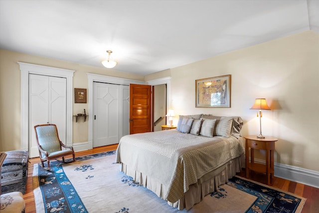 bedroom featuring multiple closets, baseboards, and wood finished floors