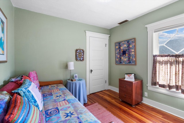 bedroom with baseboards, multiple windows, visible vents, and wood finished floors