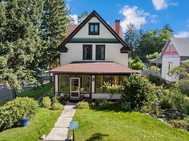 victorian-style house with a shingled roof, a chimney, and a front yard