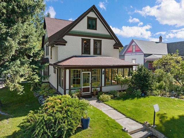 view of front facade with a sunroom, roof with shingles, and a front lawn