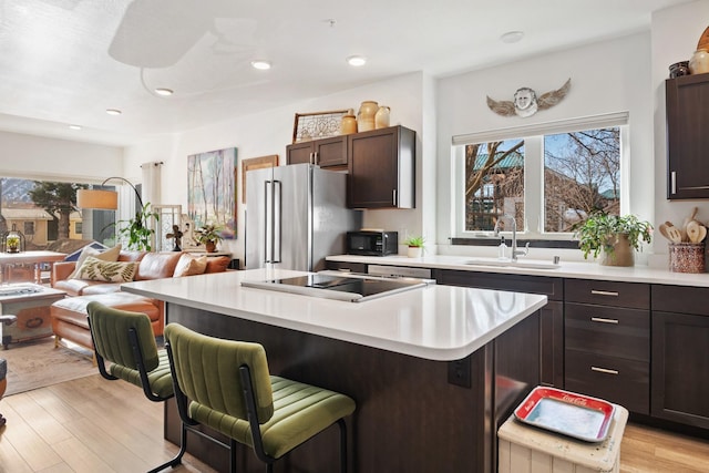 kitchen with a sink, open floor plan, high end fridge, light countertops, and a kitchen bar