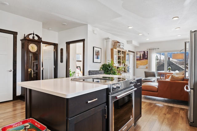 kitchen with dark brown cabinetry, light countertops, appliances with stainless steel finishes, a center island, and light wood finished floors