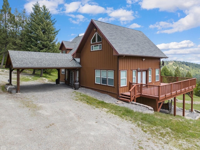 exterior space with an attached carport, roof with shingles, gravel driveway, and a wooden deck