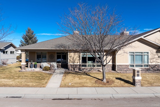 ranch-style house featuring stone siding, a shingled roof, a chimney, and a front yard