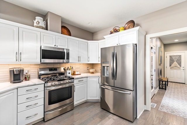 kitchen with tasteful backsplash, light wood-style flooring, appliances with stainless steel finishes, white cabinets, and light stone countertops