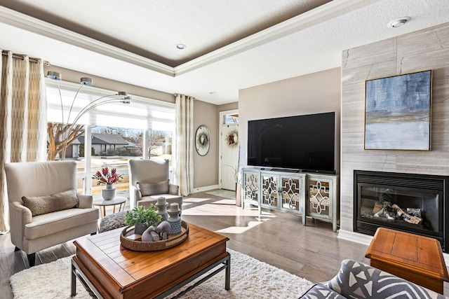 living room featuring a textured ceiling, a fireplace, wood finished floors, baseboards, and a raised ceiling