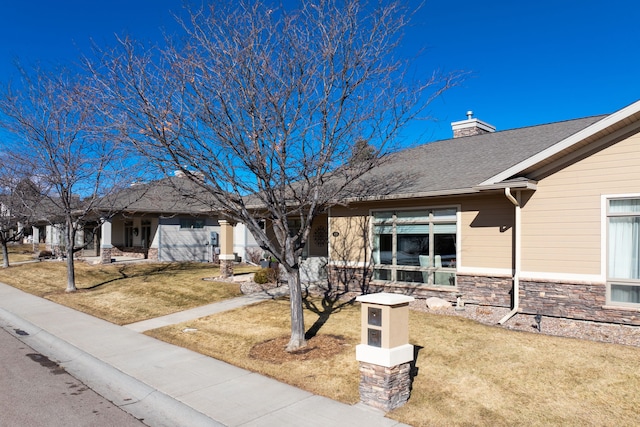 ranch-style home with stone siding, a chimney, a front lawn, and roof with shingles