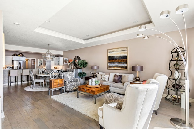 living area with a textured ceiling, wood finished floors, a raised ceiling, and an inviting chandelier