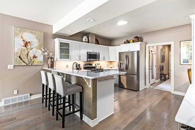 kitchen featuring visible vents, decorative backsplash, appliances with stainless steel finishes, glass insert cabinets, and a peninsula