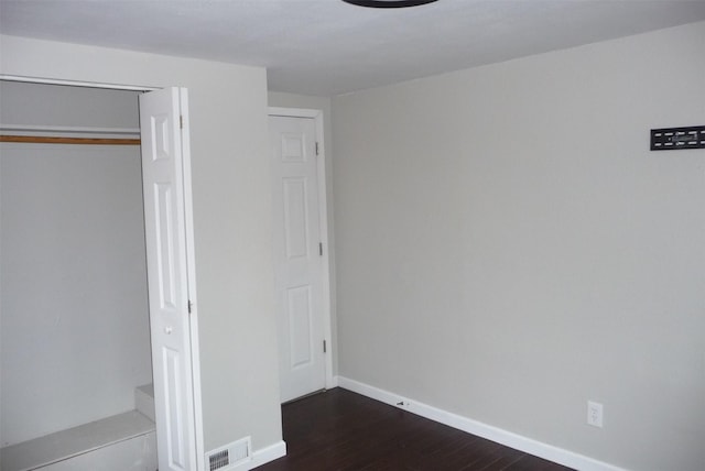 unfurnished bedroom with dark wood-style floors, a closet, visible vents, and baseboards