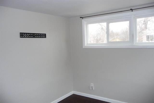 spare room featuring baseboards, dark wood finished floors, and a healthy amount of sunlight